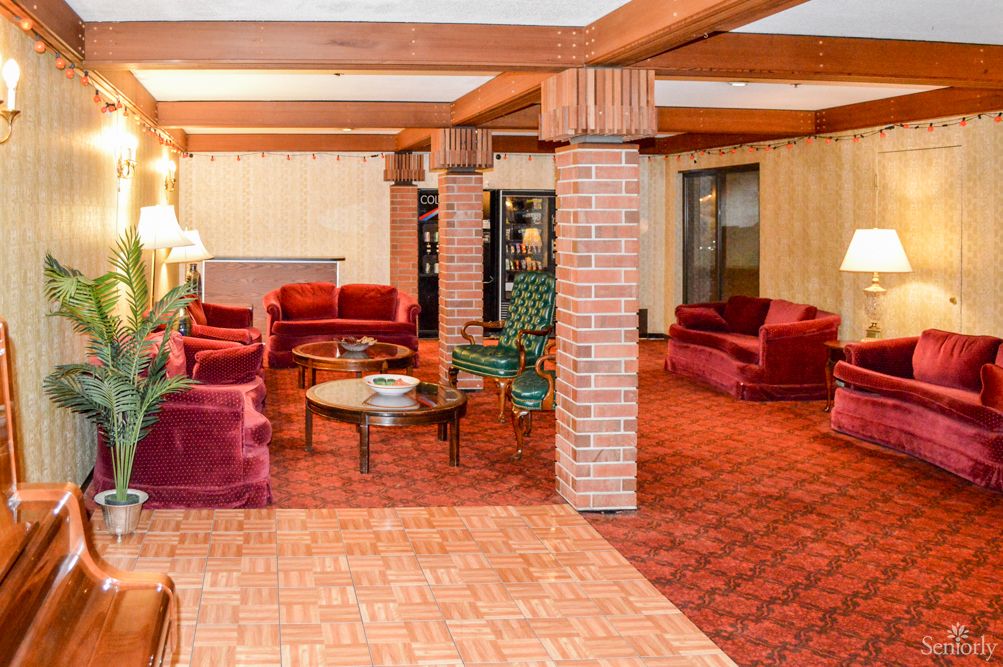 A cozy lounge with red upholstered sofas, brick pillars, and coffee tables.