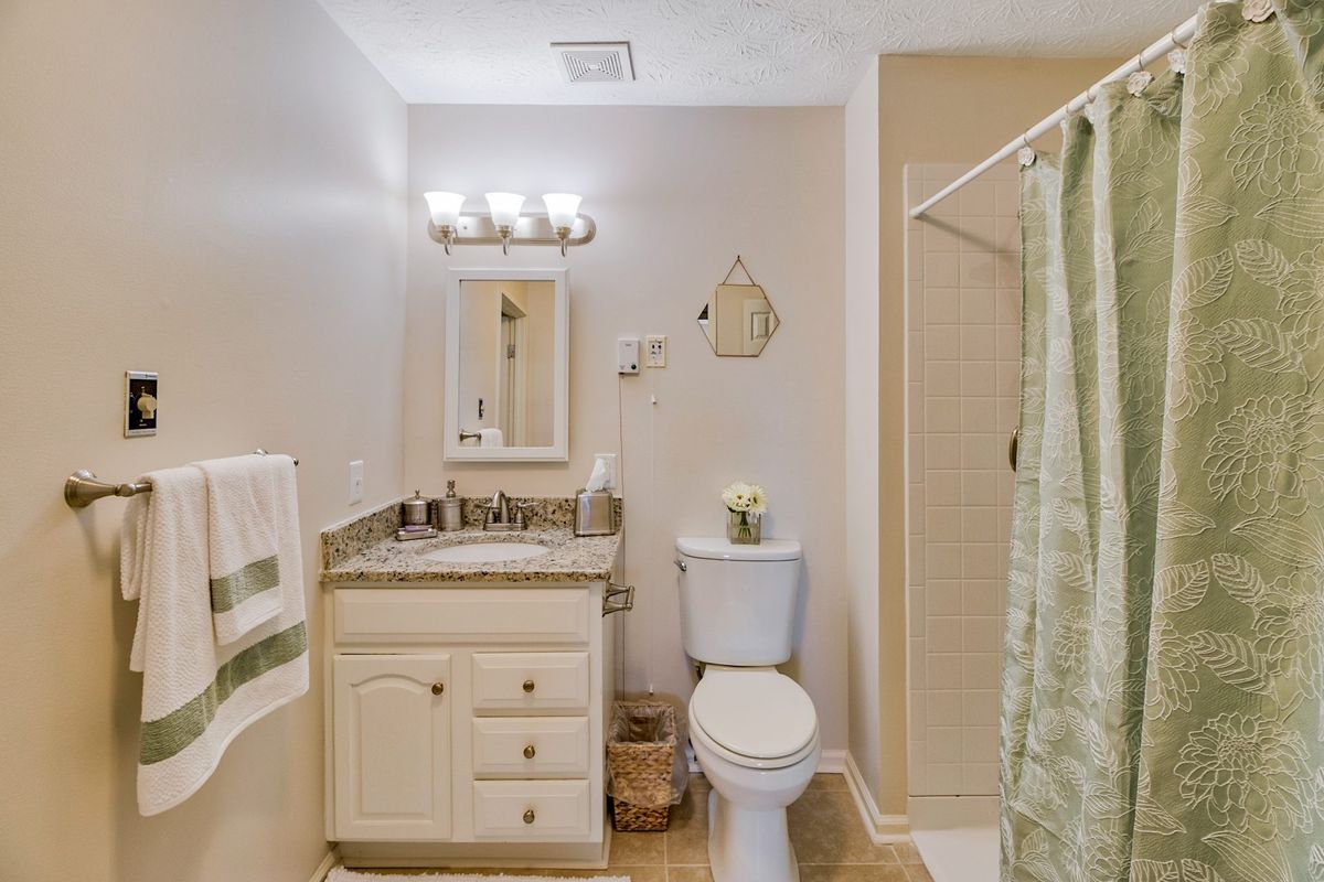 A clean and well-organized bathroom featuring a vanity with a mirror, toilet, and shower area.