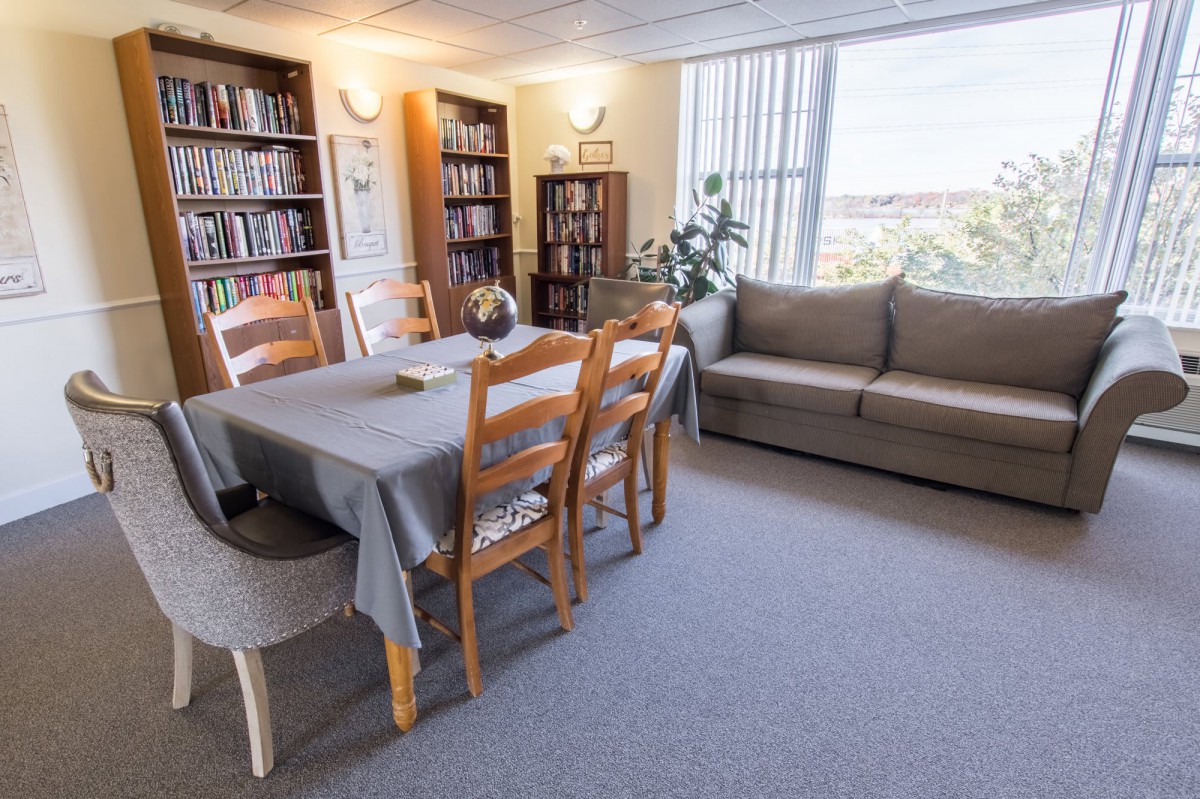 A cozy living room with a dining area, featuring bookshelves, a sofa, and a window with natural light.