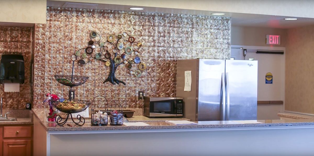 A kitchen area featuring a microwave, a large fridge, and a decorative tree sculpture on the wall.
