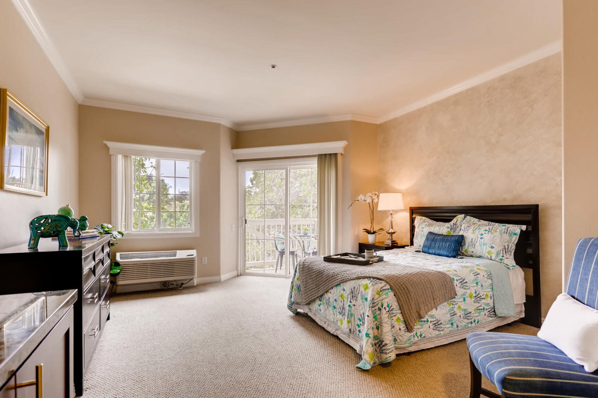 A cozy bedroom with a large bed, bedside lamp, and natural light from a window and sliding door.
