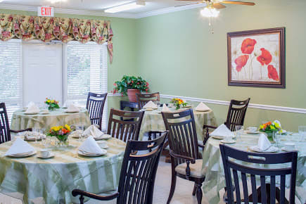 A beautifully arranged dining room with tables set for a meal, featuring green walls and floral decorations.