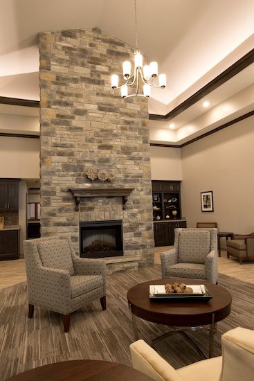 A modern living room featuring a tall stone fireplace, comfortable seating, and a stylish chandelier.