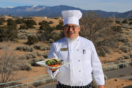 A chef proudly presents a beautifully plated dish against a scenic backdrop.