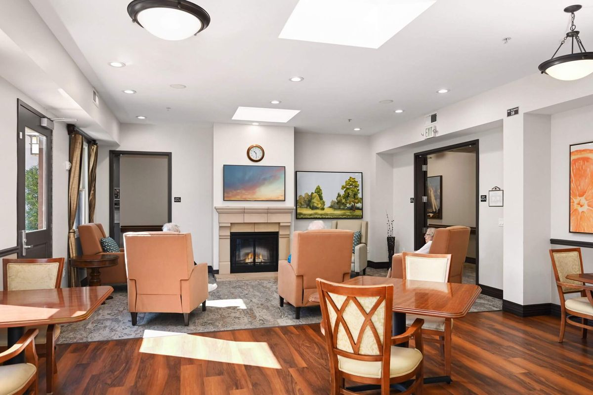 A cozy living room with comfortable seating and a fireplace, featuring hardwood floors and bright lighting.