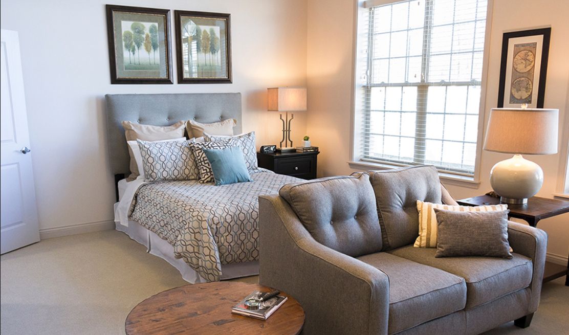 A cozy bedroom with a neatly made bed, stylish sofa, and warm lighting.