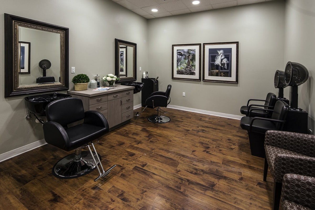 A modern hair salon interior with stylish chairs, mirrors, and framed artwork on the walls, set against a polished wooden floor.