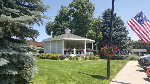 A beautifully landscaped gazebo surrounded by lush greenery and vibrant flowers on a sunny day.