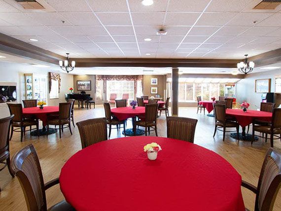 A spacious dining room with red tablecloths and a piano by the window.