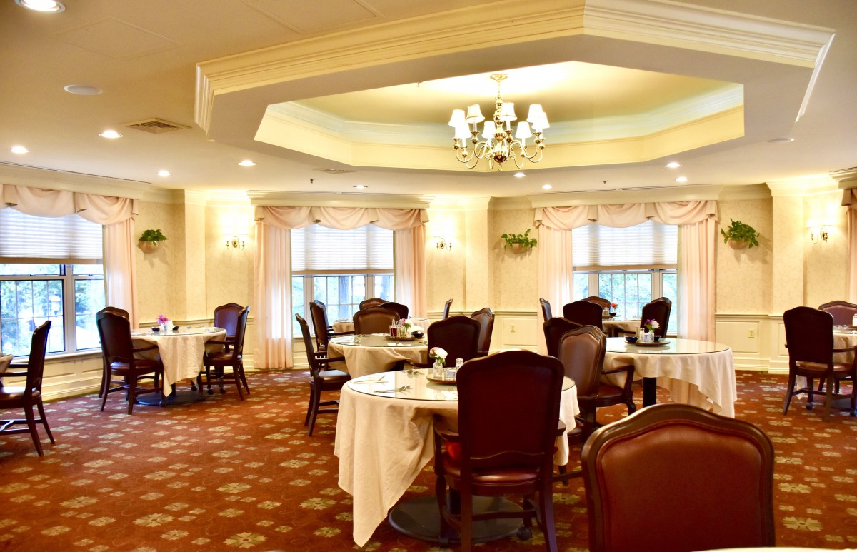 An elegant dining room with neatly arranged tables and chairs, featuring a chandelier and soft lighting.