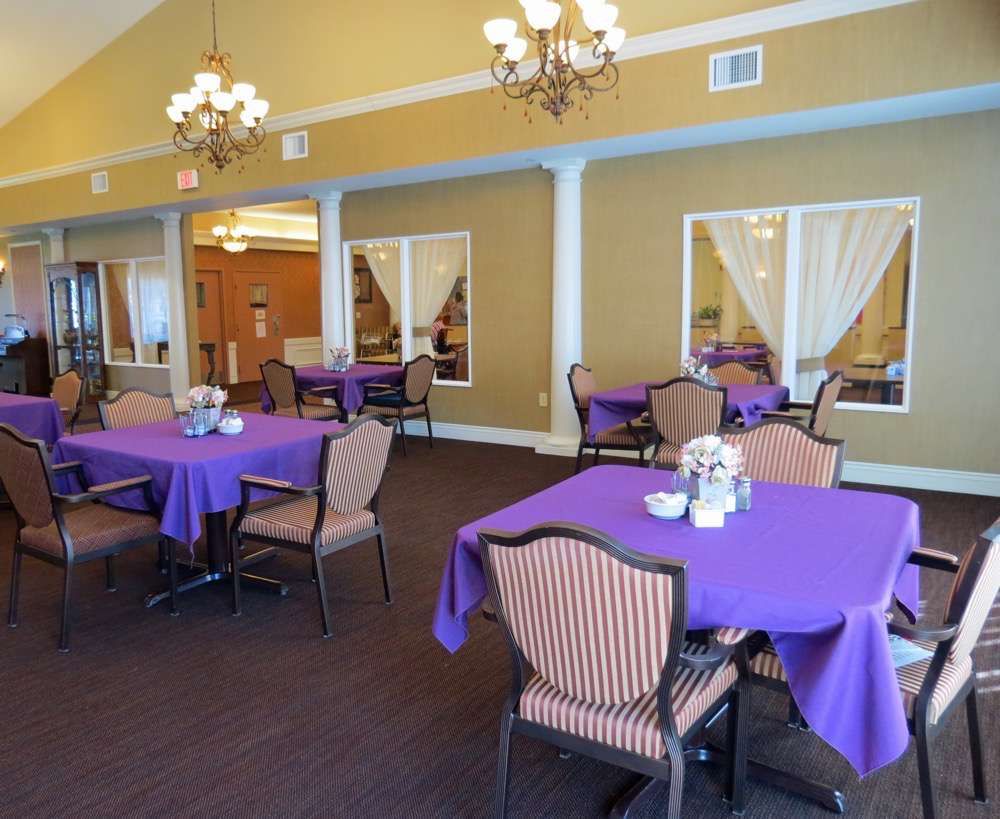 A cozy dining room featuring tables with purple tablecloths and chandeliers.