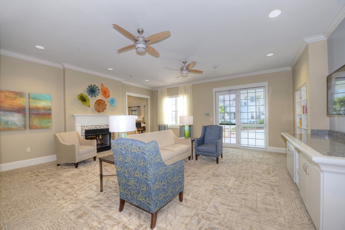 A cozy living room featuring comfortable seating, ceiling fans, and natural light from large windows.
