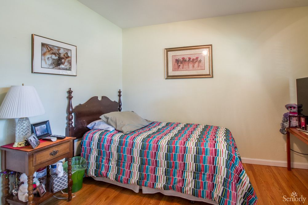 A cozy bedroom with a colorful quilt on the bed, decorated with paintings and hardwood flooring.