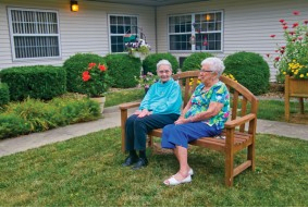 Two elderly individuals sitting on a bench in a garden, enjoying each other's company.