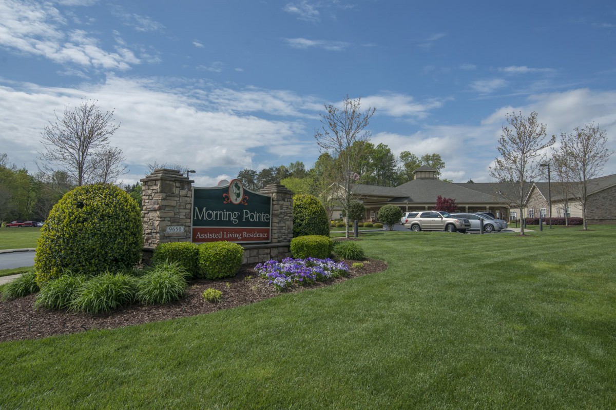 A well-maintained garden with a sign and building in the background under a partly cloudy sky.