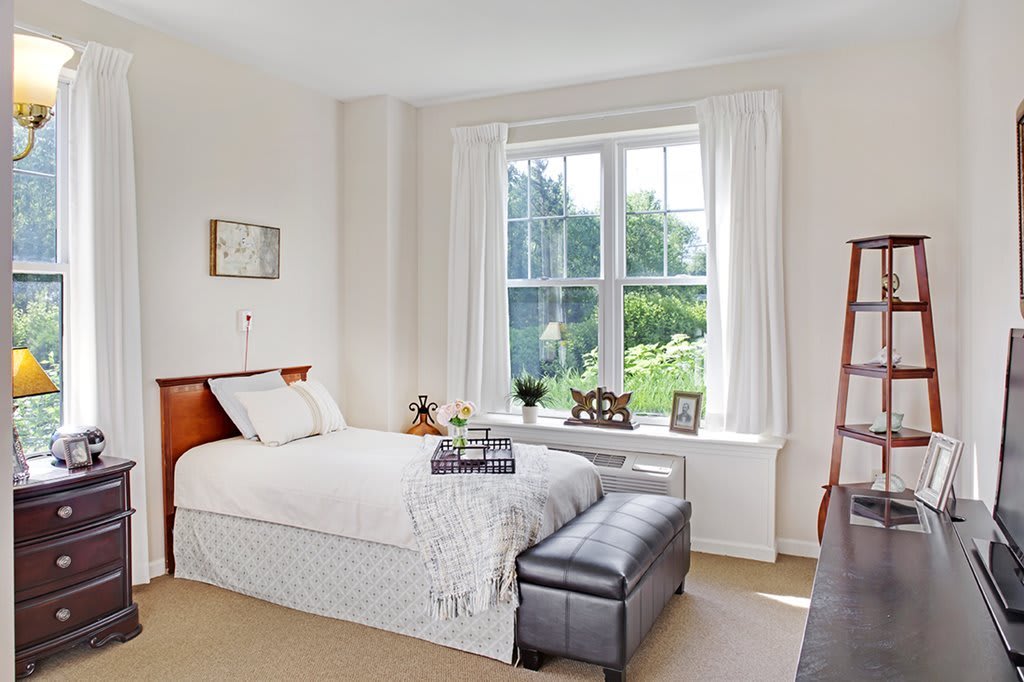 A cozy bedroom with a neatly made bed and large window allowing natural light to fill the room.