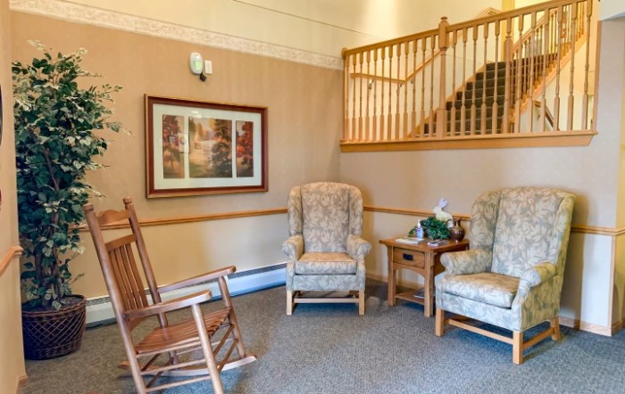 A cozy living room corner featuring a rocking chair, two armchairs, and a side table near a staircase.