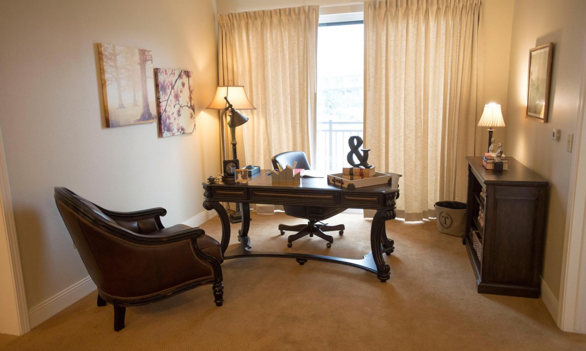 A well-furnished office space with a classic wooden desk and chair, complemented by soft lighting and beige curtains.