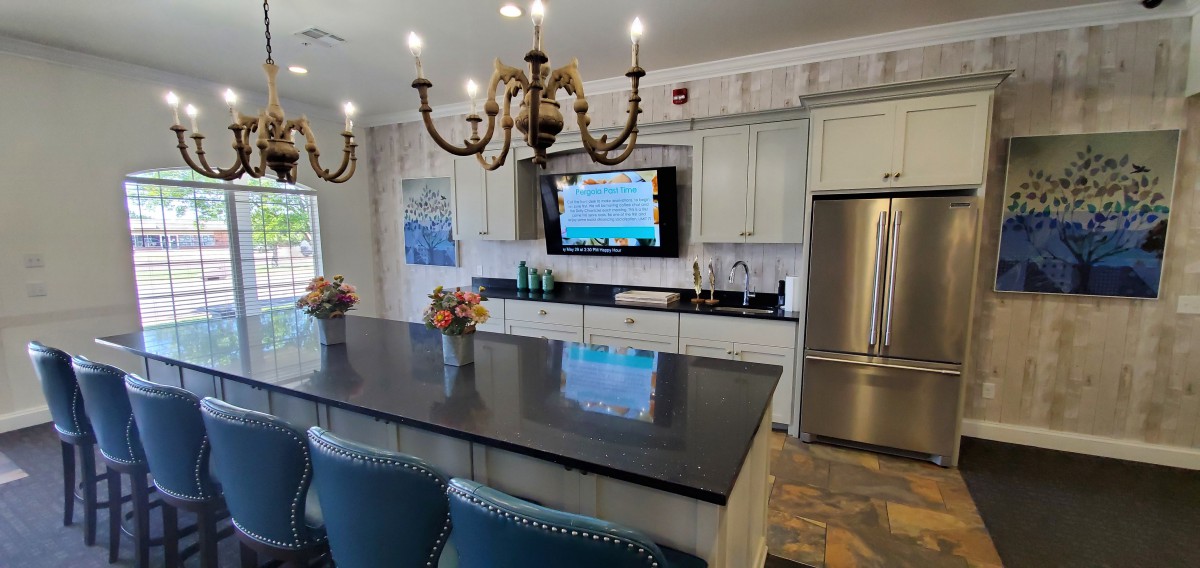 A modern kitchen with a large island, elegant chandelier, and sleek appliances.
