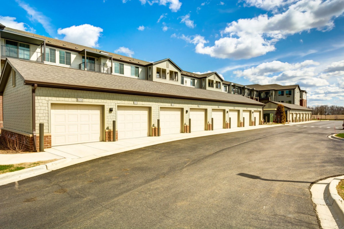 A modern apartment complex with multiple garage doors under a bright, cloudy sky.
