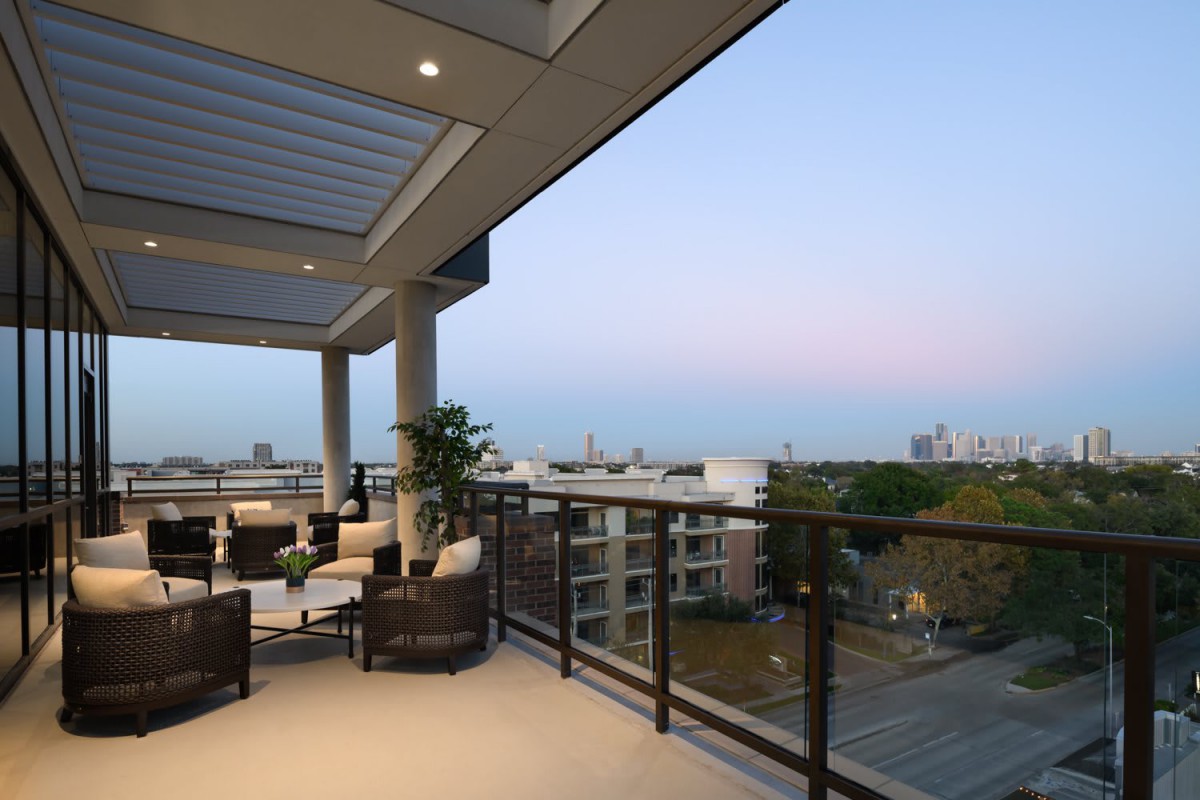 A spacious balcony with comfortable seating overlooking a cityscape at dusk.
