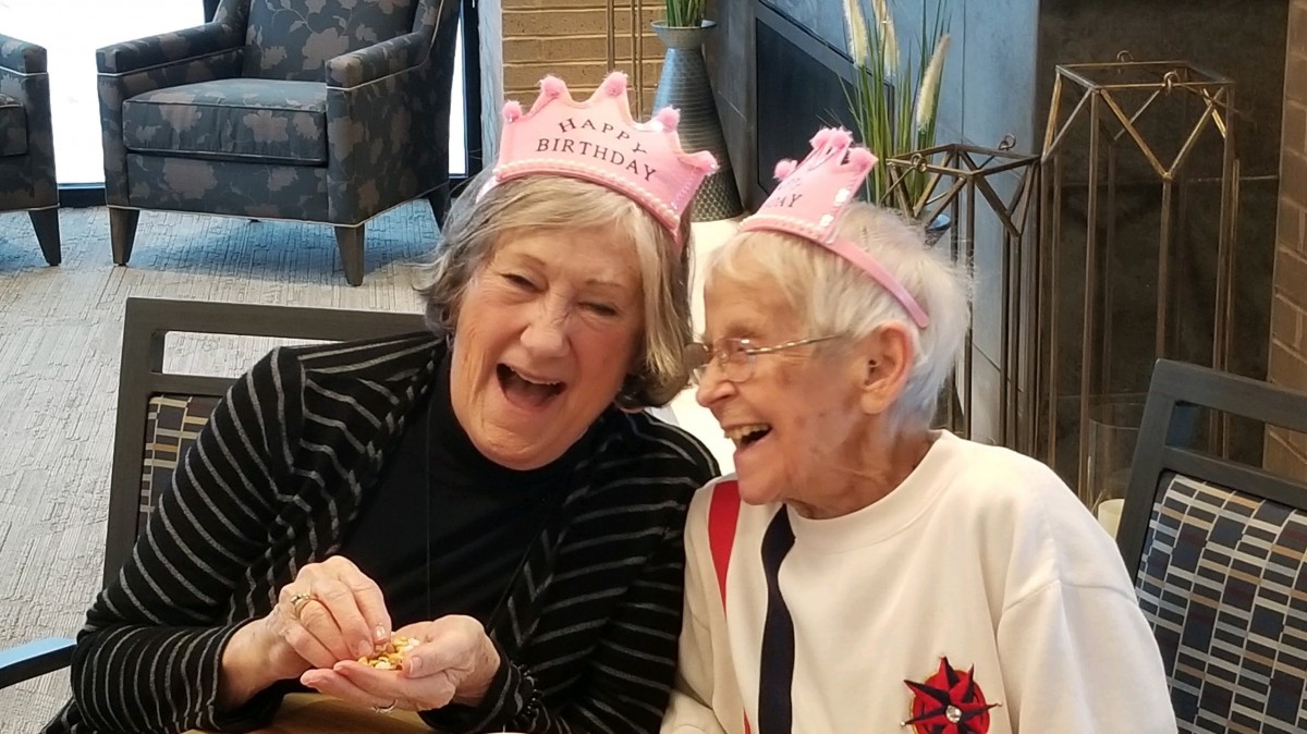 Two elderly women joyfully celebrating a birthday with pink hats.