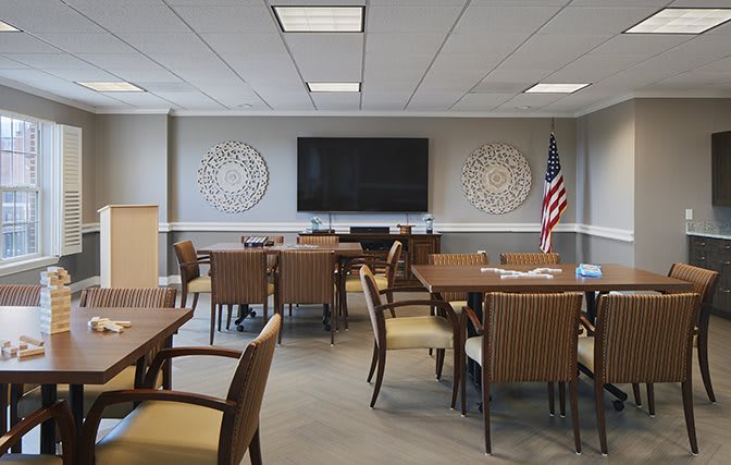 A modern conference room with tables, chairs, a large screen, and an American flag.