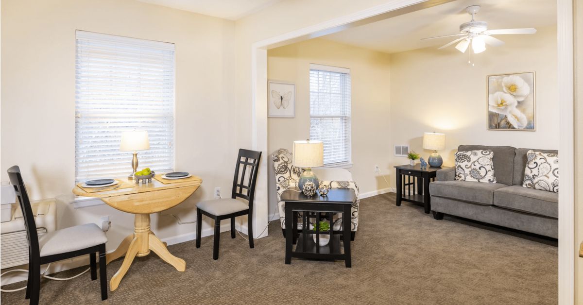 A modern living room with light-colored walls, carpeted floors, and minimalist furnishings.