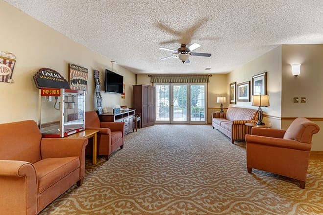 A spacious living room with comfortable seating and a television, featuring a large window and carpeted floor.