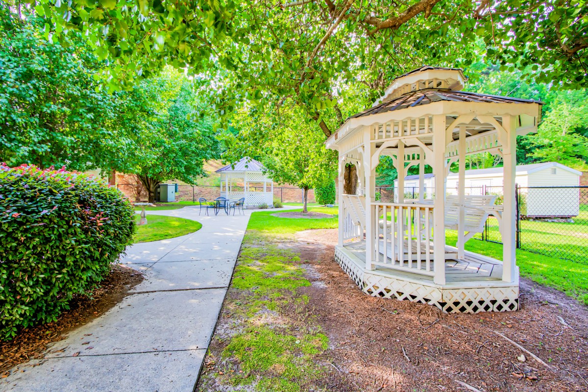 A peaceful garden setting featuring a white gazebo surrounded by lush greenery and a winding pathway.