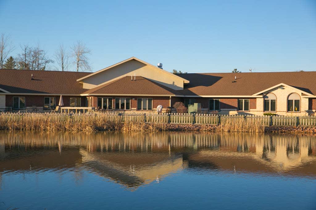 A house by a calm lake with its reflection visible in the water.