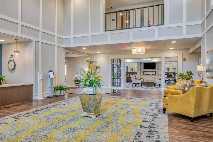 A modern lobby with elegant decor, featuring a central table with flowers, a chandelier, and comfortable seating.