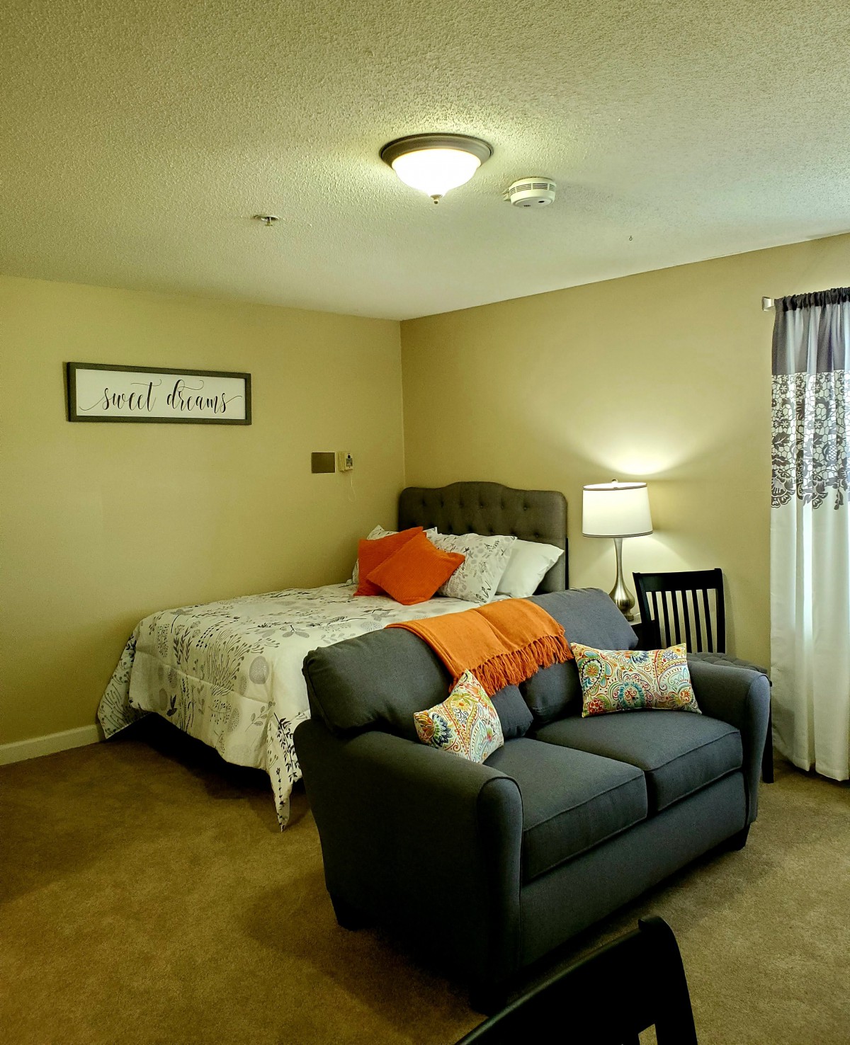 A cozy bedroom with a bed, sofa, and lamp creating a warm atmosphere.