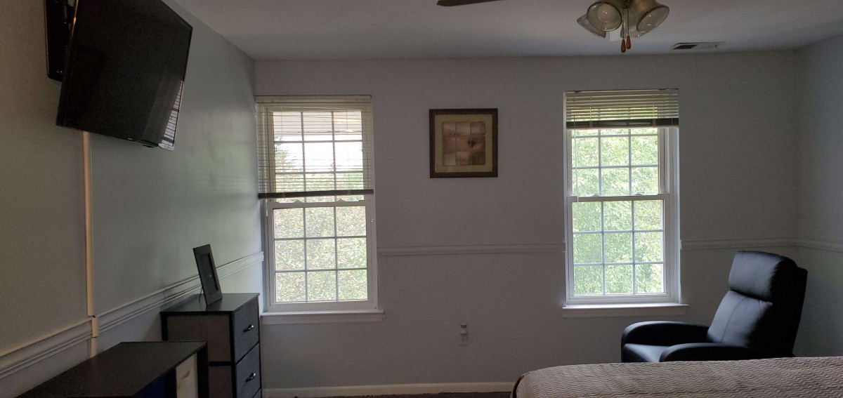 A bedroom with two windows, a dresser, and framed artwork on the wall.