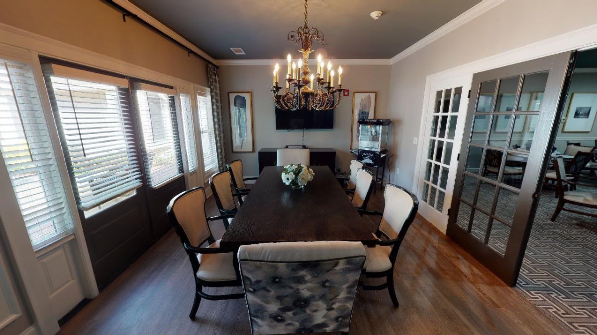 A modern dining room featuring a large dark wood table, elegant chairs, a chandelier, and natural light from multiple windows.