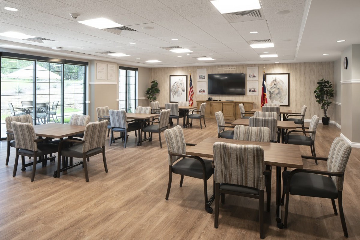 A modern dining or meeting room with neatly arranged tables and chairs, featuring a television on the wall.