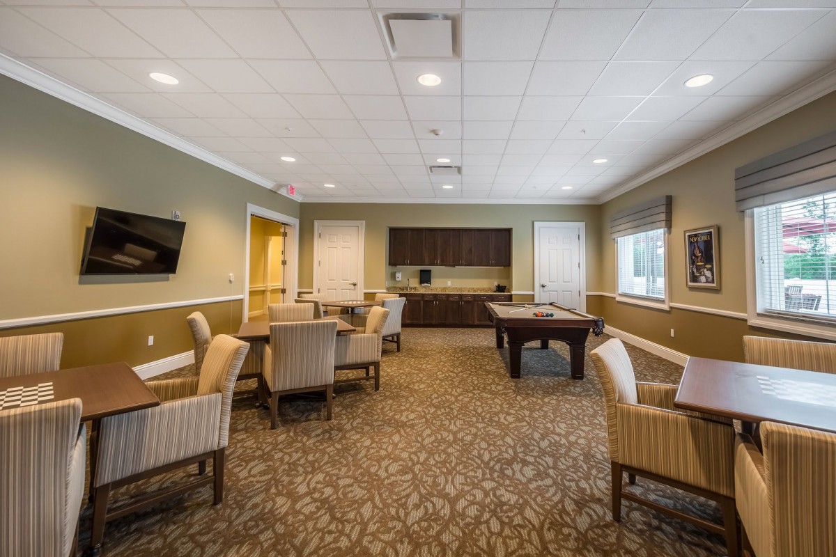 A spacious community room featuring a pool table, multiple seating arrangements, and a wall-mounted television.