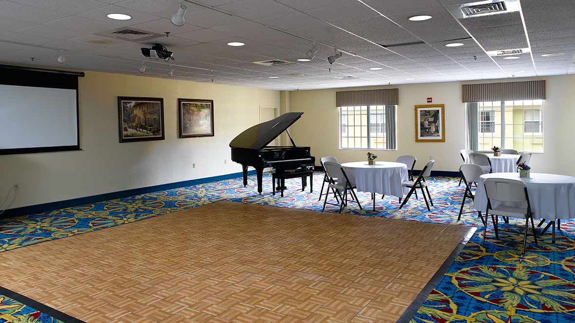 A room with a grand piano, round table, and chairs, decorated with artwork on the walls.