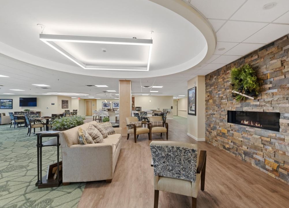 A modern lounge area featuring comfortable seating, a stone fireplace, and ample natural light.
