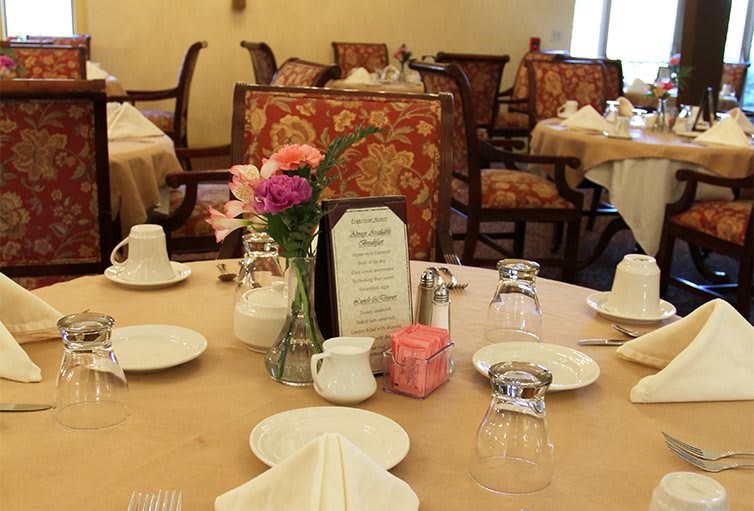An elegantly set table in a restaurant dining room, complete with flowers and a menu.