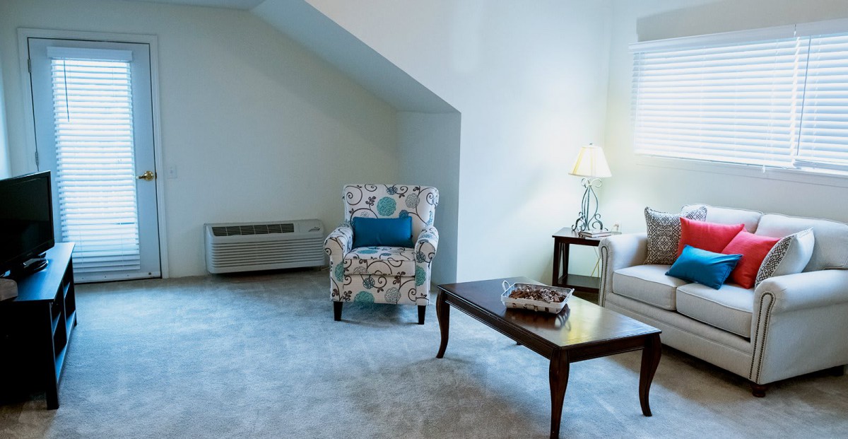 A cozy living room with a patterned armchair, coffee table, and a lamp providing soft lighting.