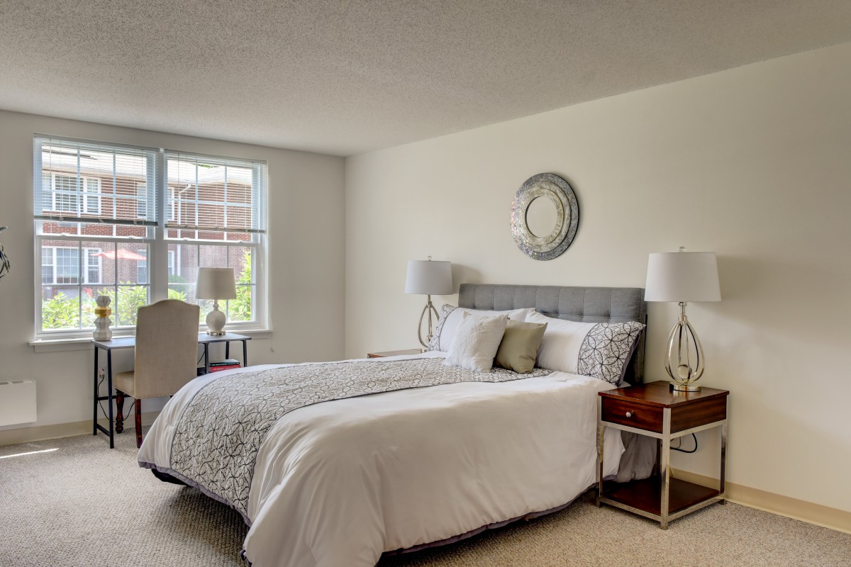 A modern bedroom with neutral tones, featuring a cozy bed, stylish nightstands with lamps, and a large window providing natural light.