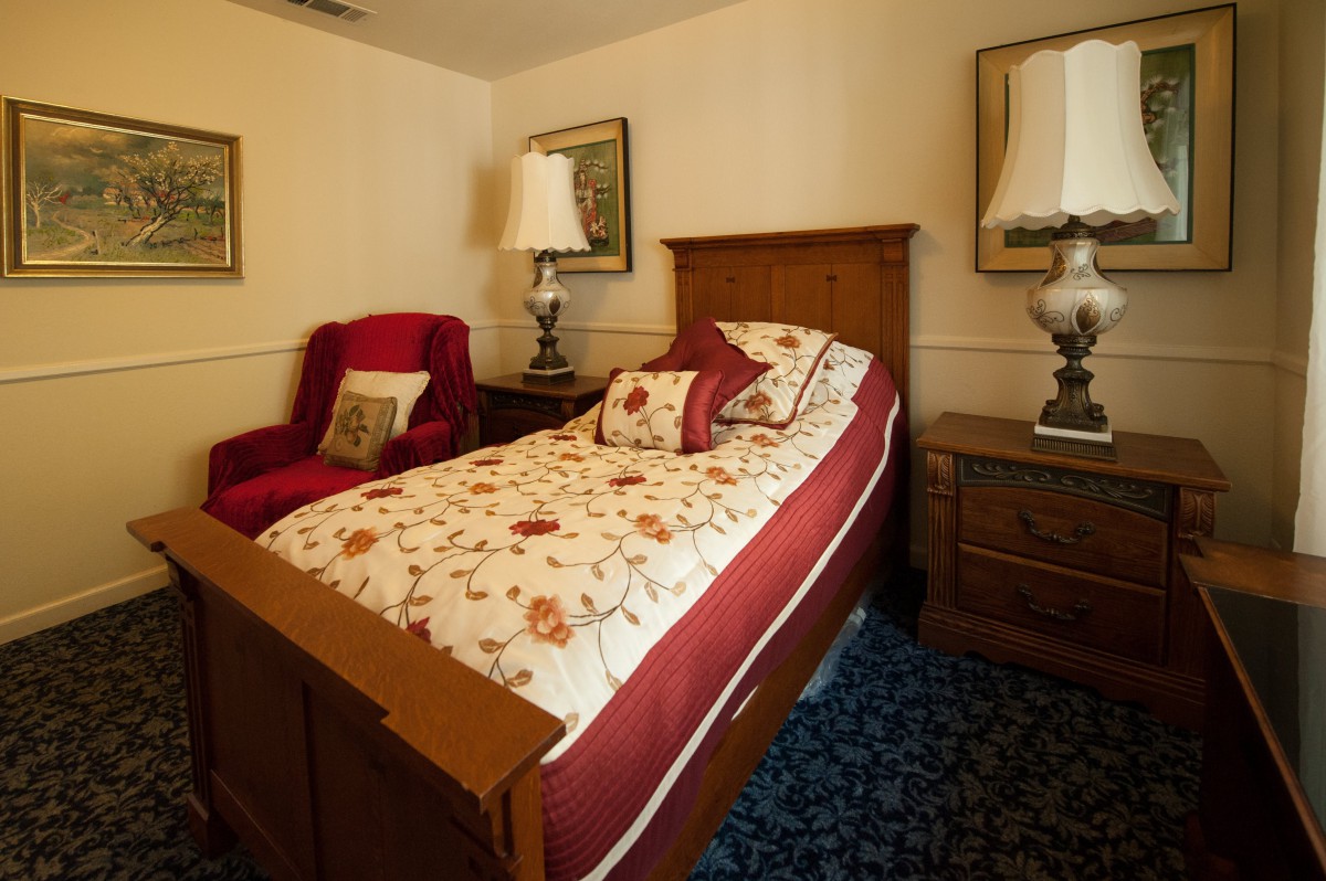 A cozy bedroom with a single bed adorned with floral bedding, accompanied by two nightstands and table lamps. An armchair adds comfort to the room.