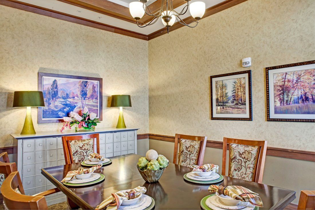 A warmly decorated dining room with a set table, featuring elegant chairs and artwork on the walls.