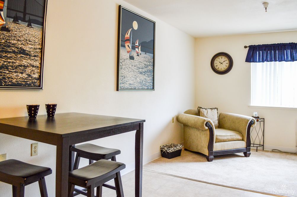 A cozy living room with a comfortable armchair, artwork on the wall, and a small table with chairs.