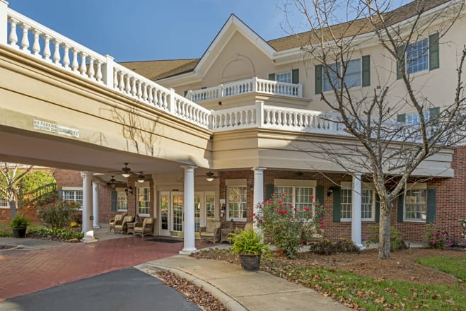 A residential building with a covered entrance and white columns, surrounded by landscaping.