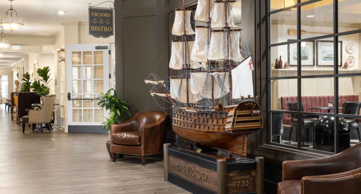 A model ship displayed indoors alongside a leather chair and plant, creating a nautical-themed decor.