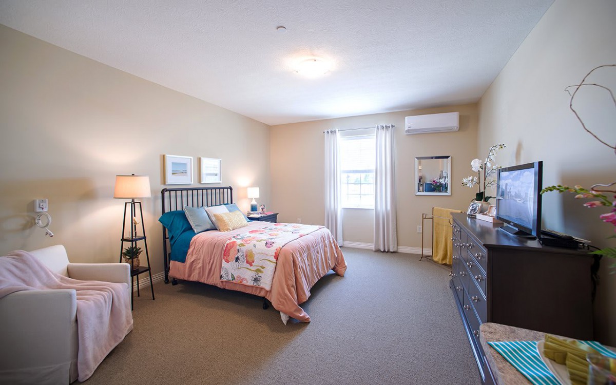 A well-decorated bedroom featuring a bed with colorful bedding, lamps, and ample natural light from the window.