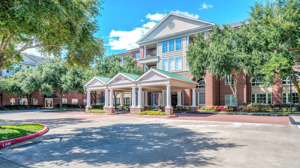 A sunny day view of a hotel entrance with surrounding trees.