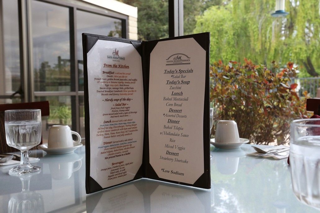 A restaurant menu displayed on a table with cups in the background.
